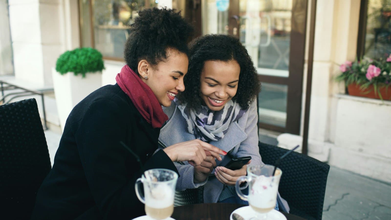 Two friends at a cafe table looking at a smartphone together