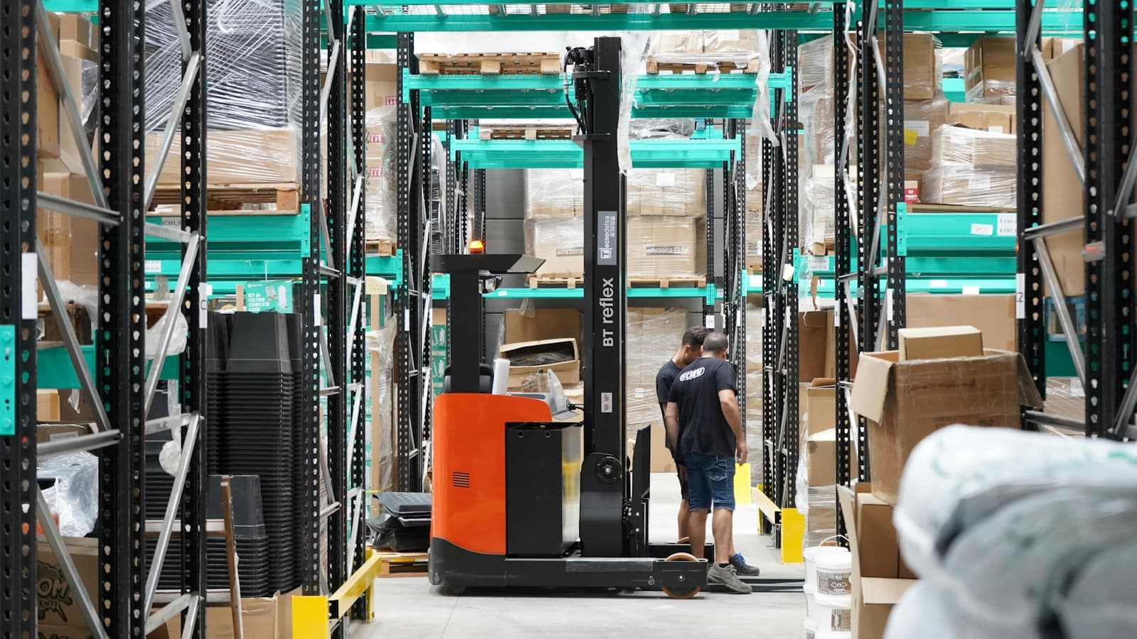Two workers beside a reach truck in a racked distribution warehouse
